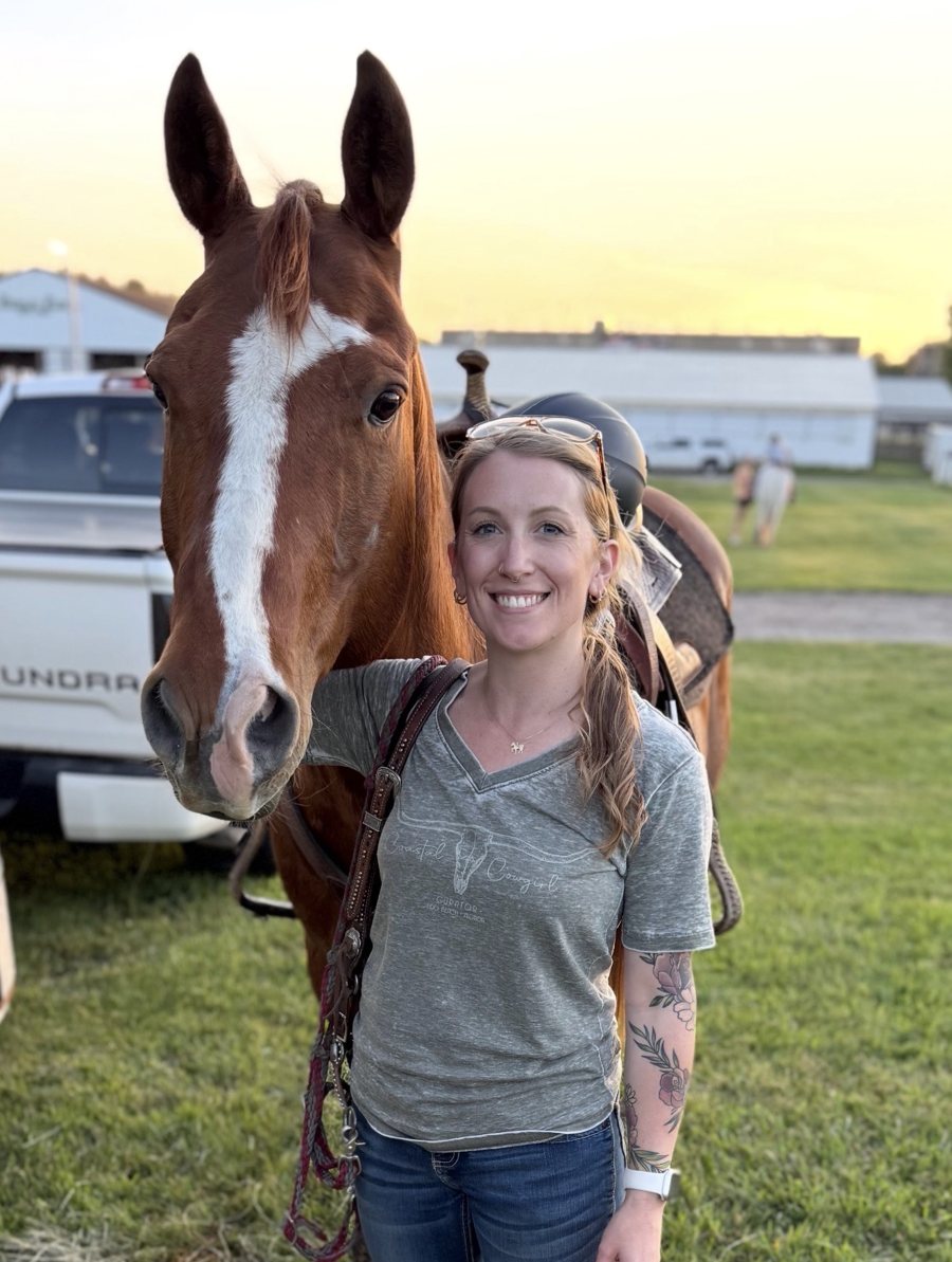 Liz standing beside her chestnut horse at the fairgrounds at sunset